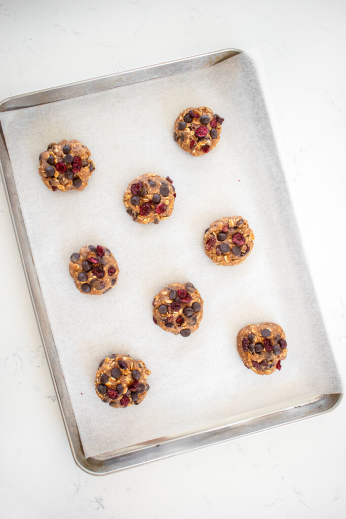 eggless oatmeal raisin chocolate chip cookie dough on a baking sheet on a white marble countertop.