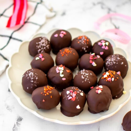 eggless red velvet sourdough cake balls with pink sprinkles on a plate on a white marble table.