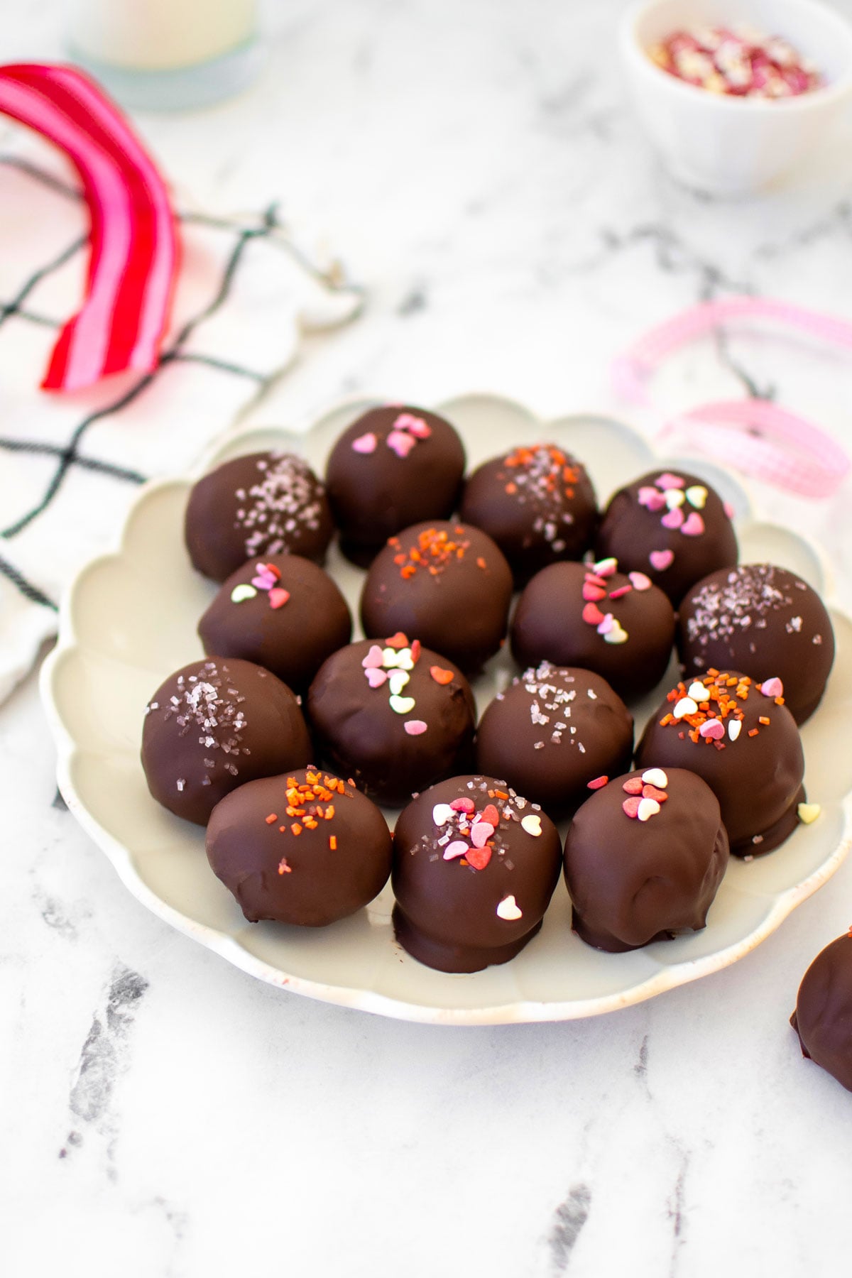 eggless red velvet sourdough cake balls with pink sprinkles on a plate on a white marble table.