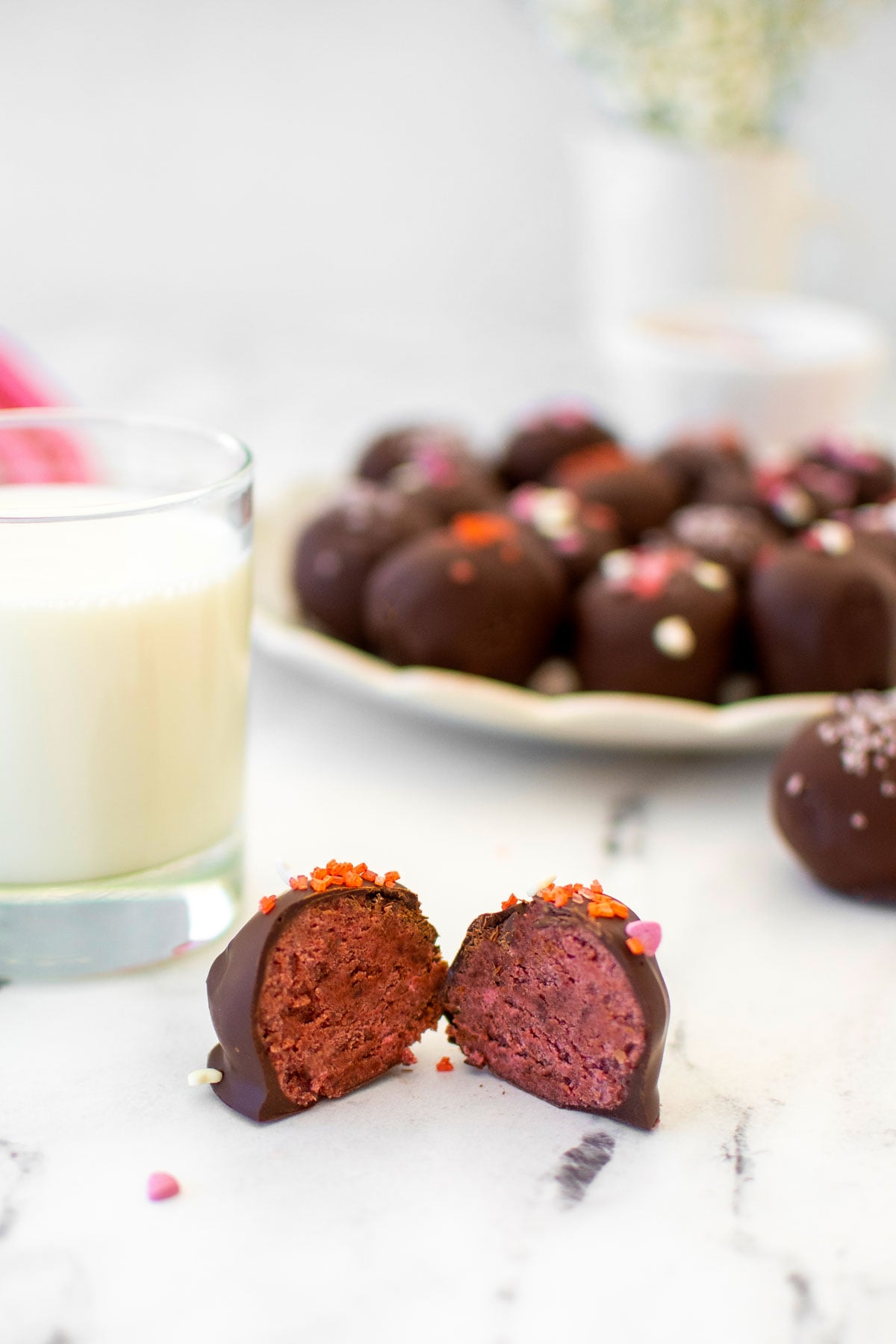 eggless red velvet sourdough cake ball cut in half on a white marble counter with a glass of milk.