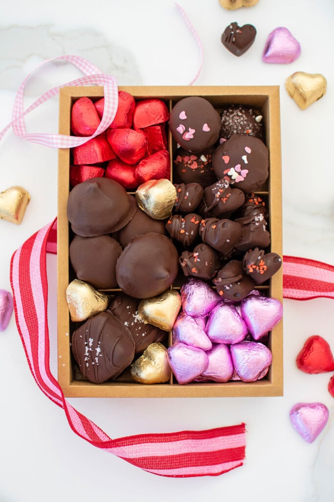 homemade valentine's day chocolate box with different chocolates and chocolate hearts on a white marble counter.