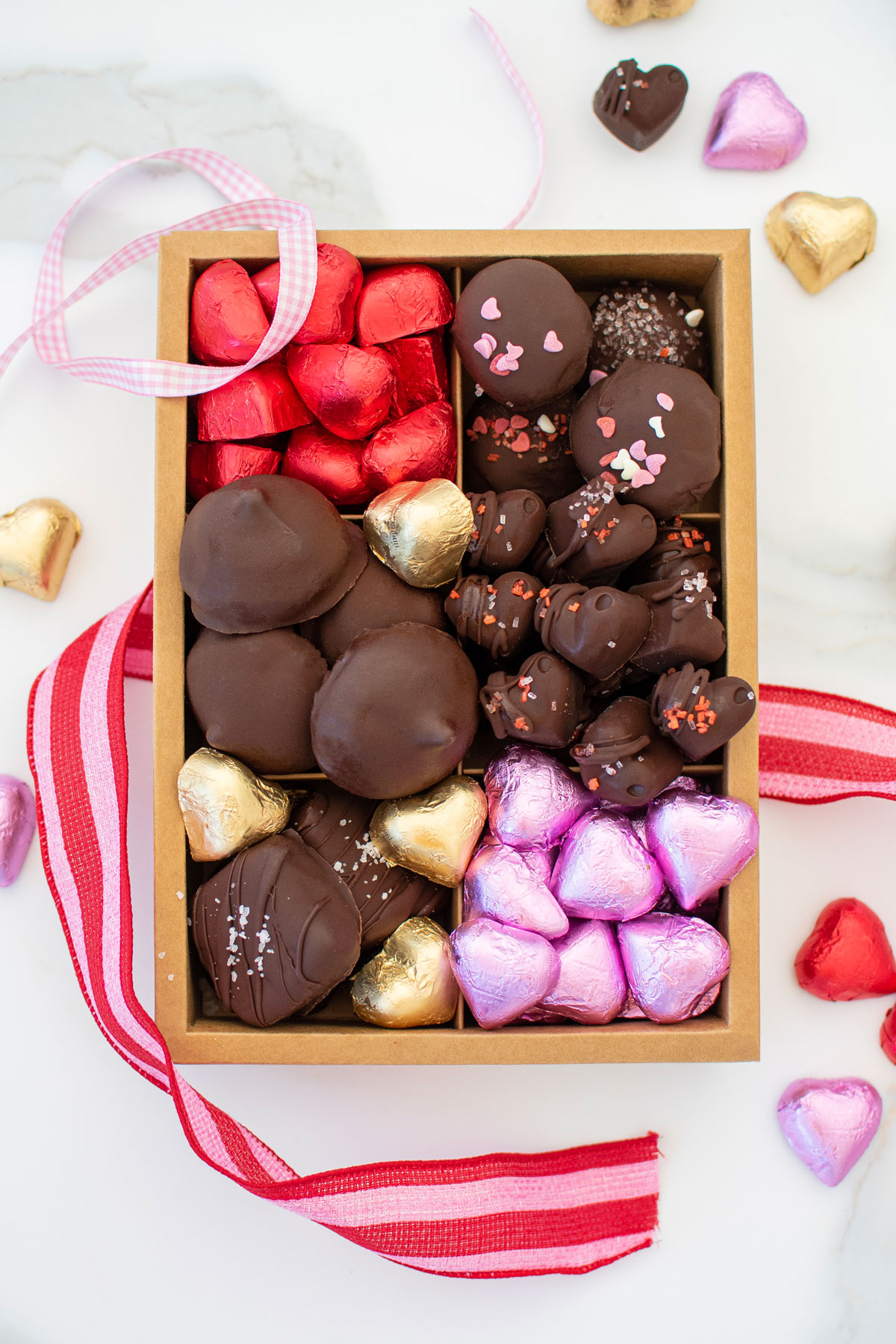 homemade valentine's day chocolate box with different chocolates and chocolate hearts on a white marble counter.