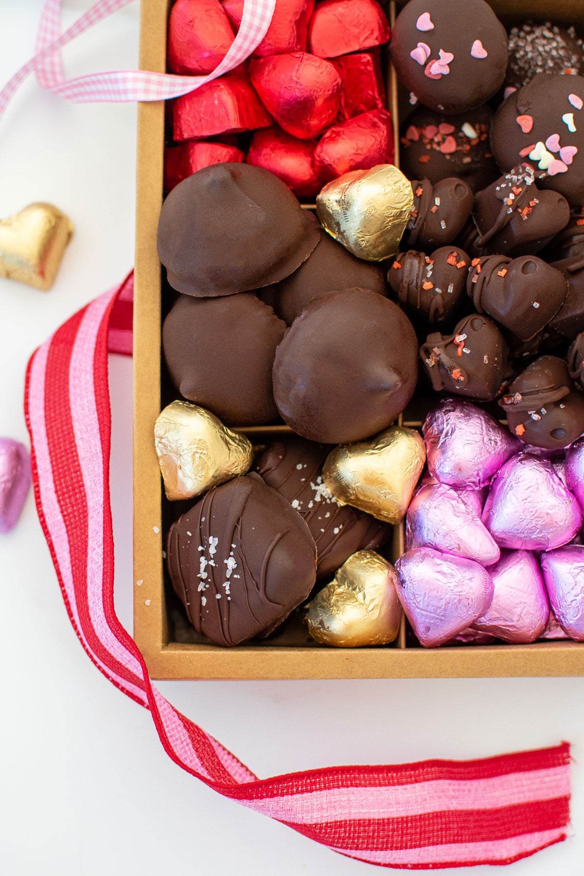 homemade valentine's day chocolate box with different chocolates and chocolate hearts on a white marble counter.