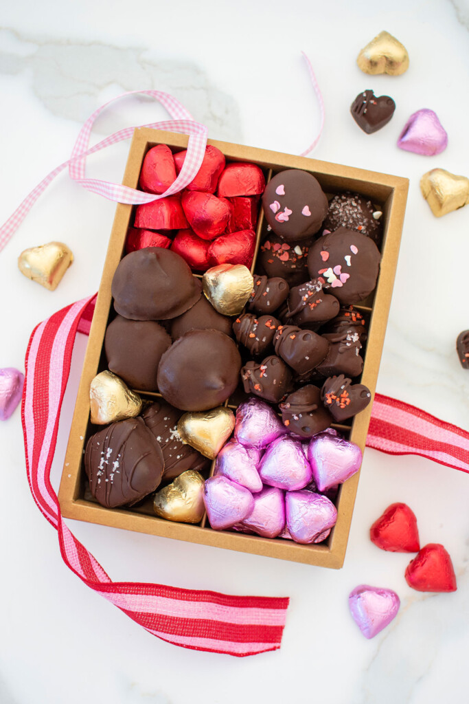 homemade valentine's day chocolate box with different chocolates and chocolate hearts on a white marble counter.