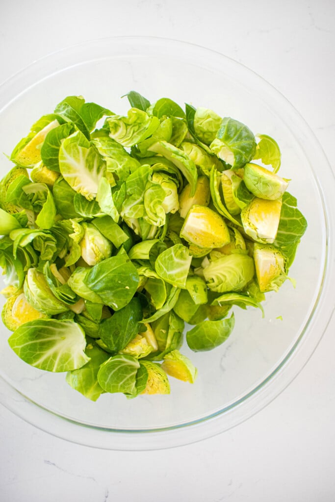 glass bowl of brusselss sprouts cut in half on a white marble countertop.
