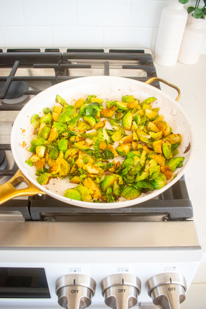 sesame ginger brussels sprouts cooking in a large skillet over the stovetop.