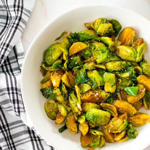 bowl of sesame ginger brussels sprous on a white marble countertop.