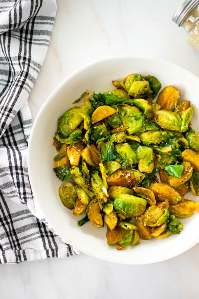 bowl of sesame ginger brussels sprous on a white marble countertop.
