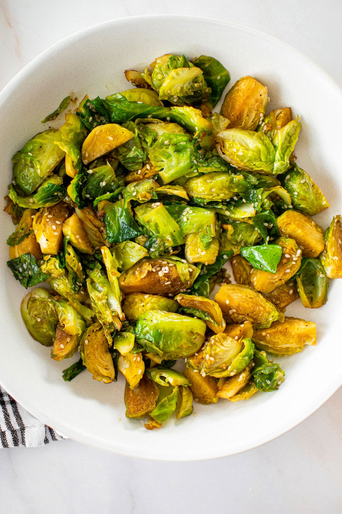 Sesame ginger Brussels sprouts without soy, caramelized in olive oil with ginger in a bowl on a white marble countertop.