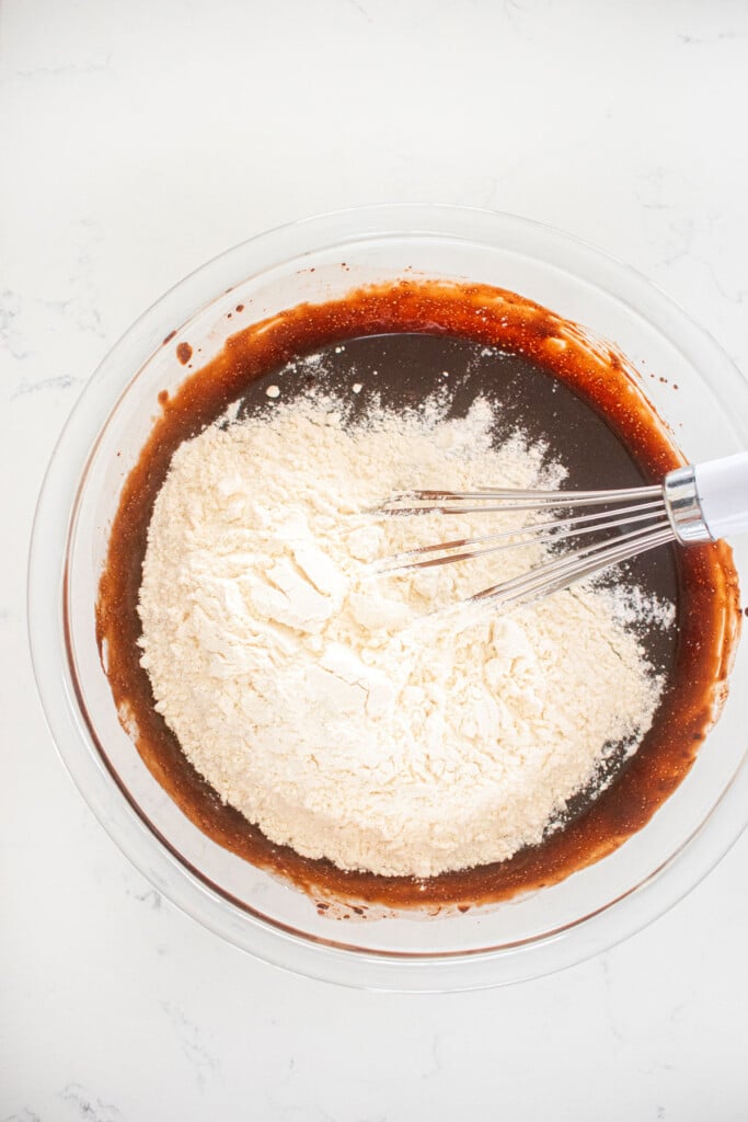 ingredients for sourdough chocolate chip brownie batter in a glass mixing bowl on a white marble counter.