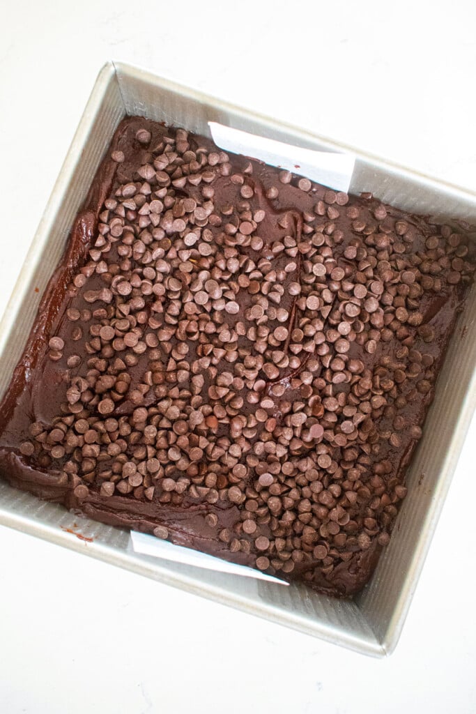 sourdough chocolate chip brownie batter in a square baking pan on a white marble counter.