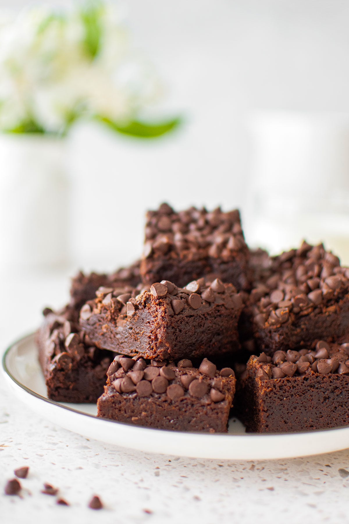 sourdough chocolate chip brownies on a plate on a white stone counter with fresh flowers.