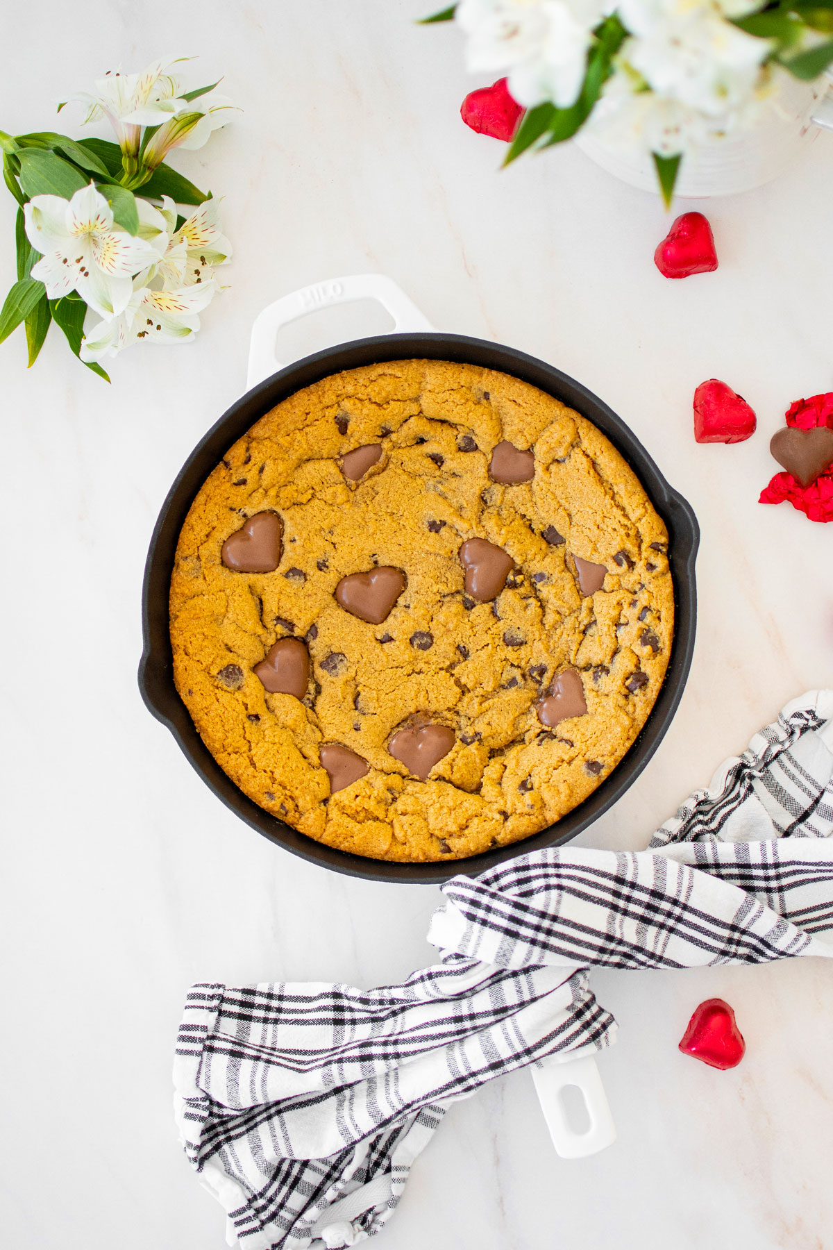 valentine's day peanut butter cookie skillet with chocolate hearts on a marble counter with fresh flowers.