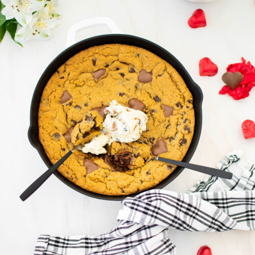 valentine's day peanut butter cookie skillet with vanilla ice cream and spoons on a marble counter.