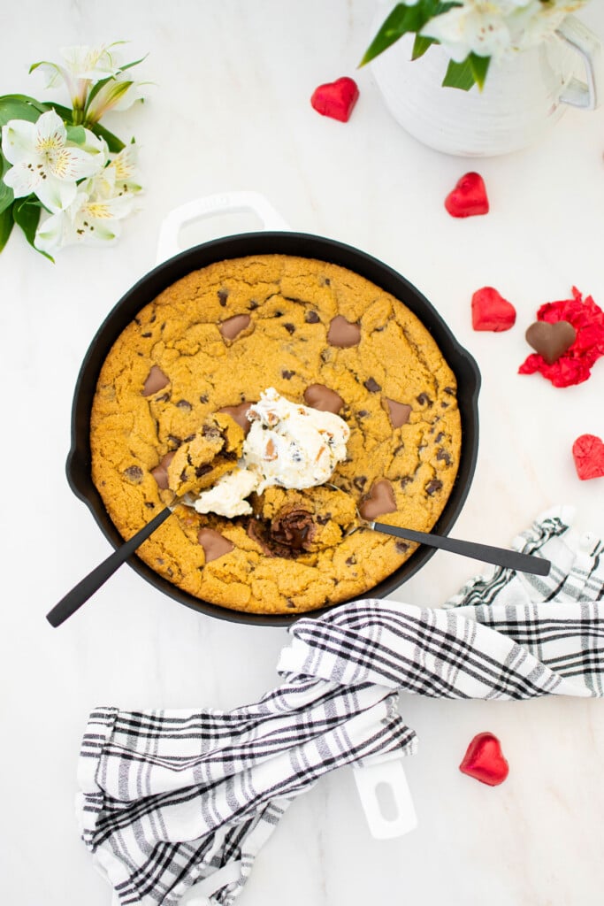 valentine's day peanut butter cookie skillet with vanilla ice cream and spoons on a marble counter.