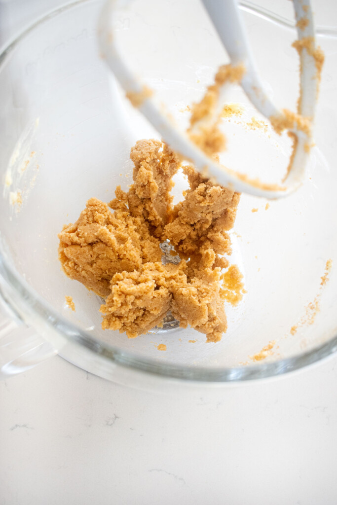 creamed butter and brown sugar in a glass stand mixing bowl on a white marble counter.