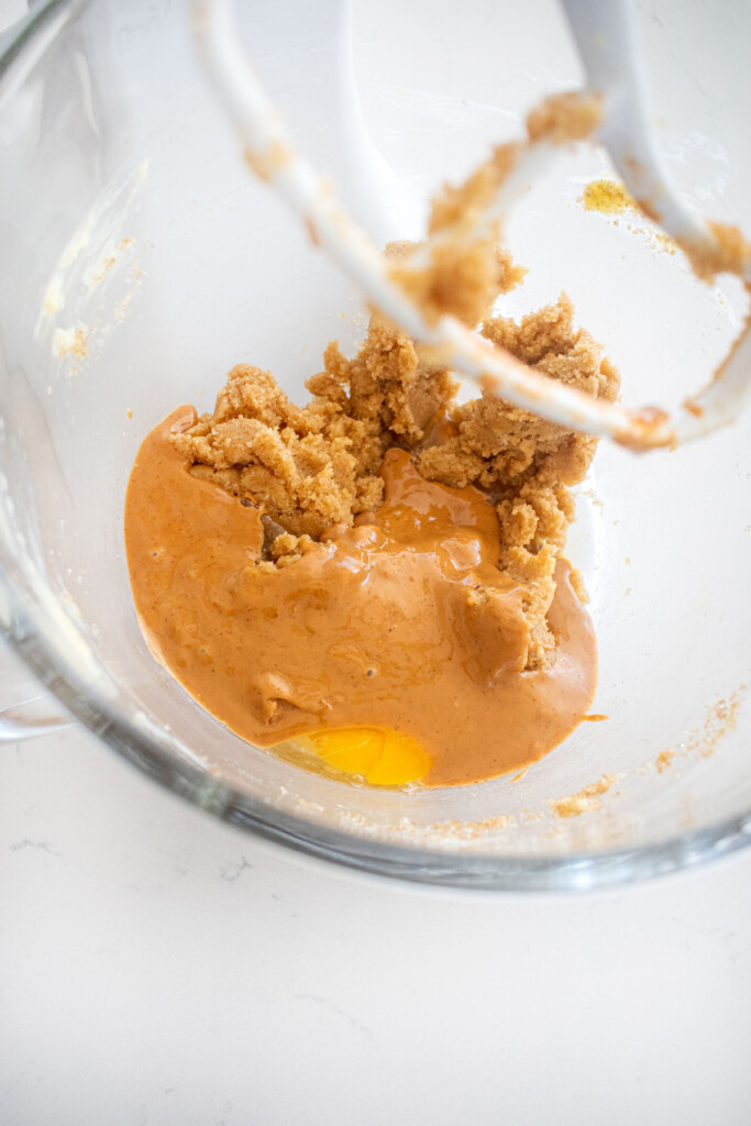wet ingredients for peanut butter cookie dough in a glass stand mixing bowl on a white marble counter.