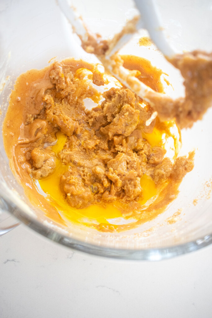 wet ingredients for peanut butter cookie dough in a glass stand mixing bowl on a white marble counter.