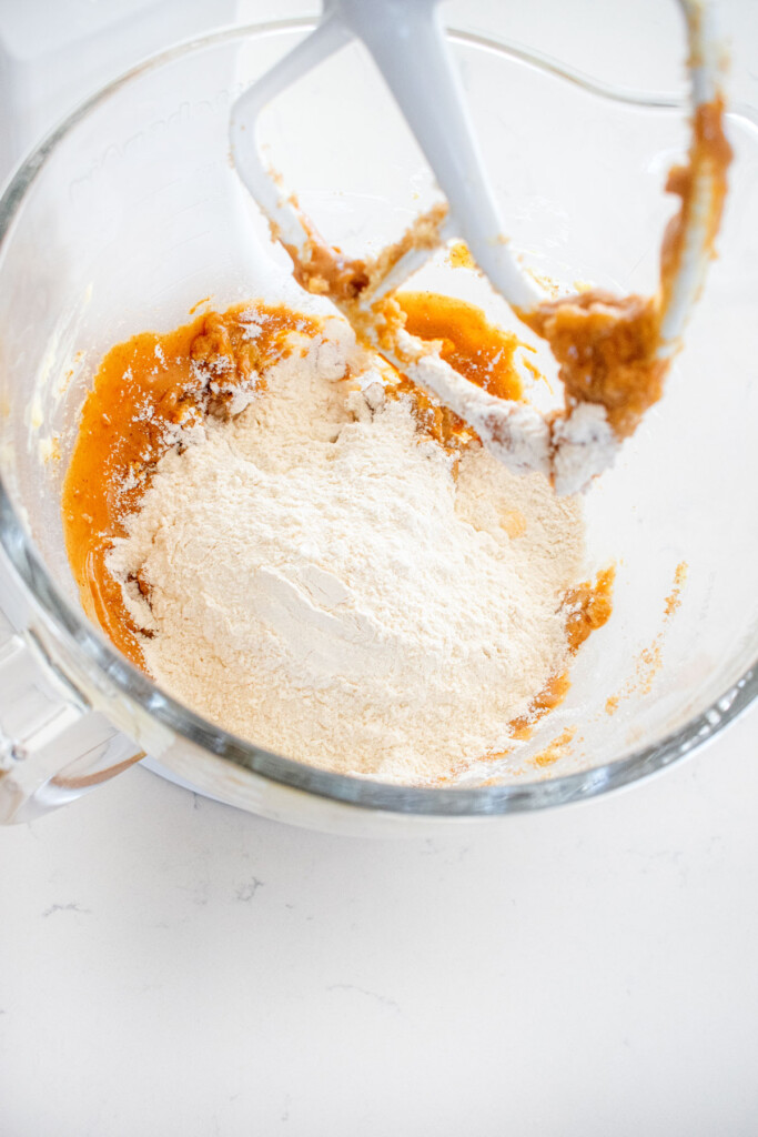 ingredients for peanut butter cookie dough in a glass stand mixing bowl on a white marble counter.