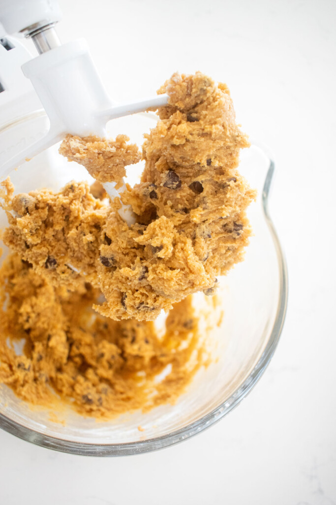 peanut butter chocolate chip cookie dough in a stand mixing bowl on a white marble counter.