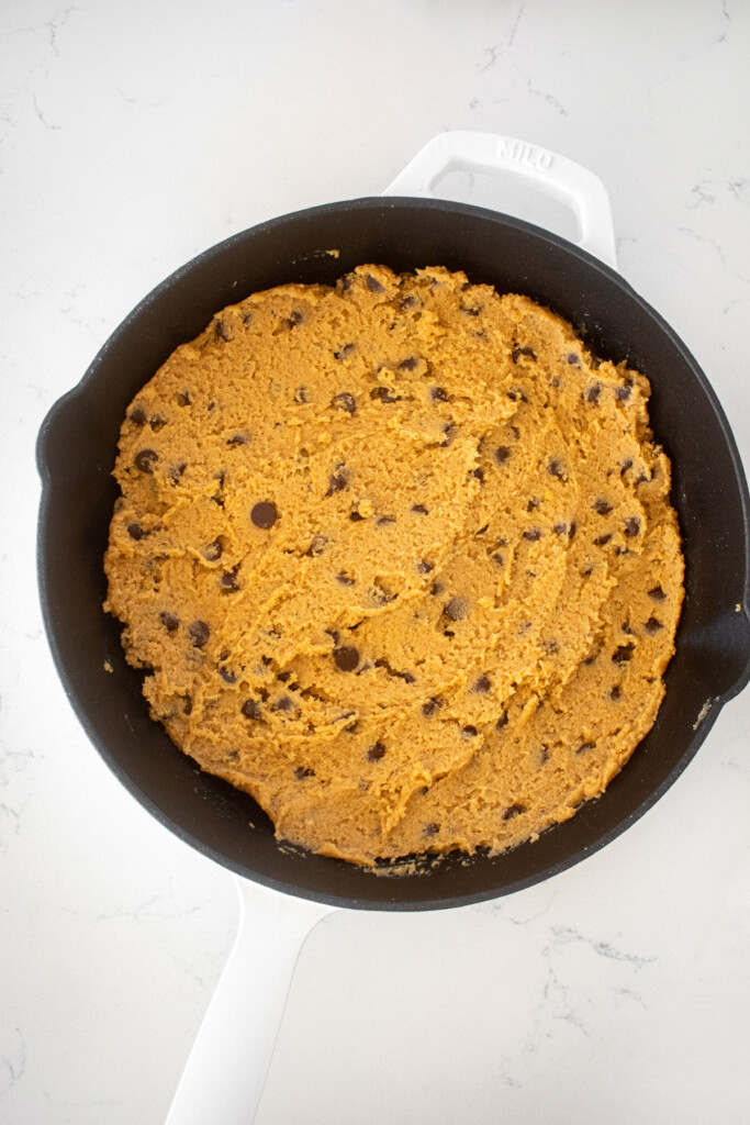 peanut butter chocolate chip cookie dough pressed into a skillet on a white marble counter.
