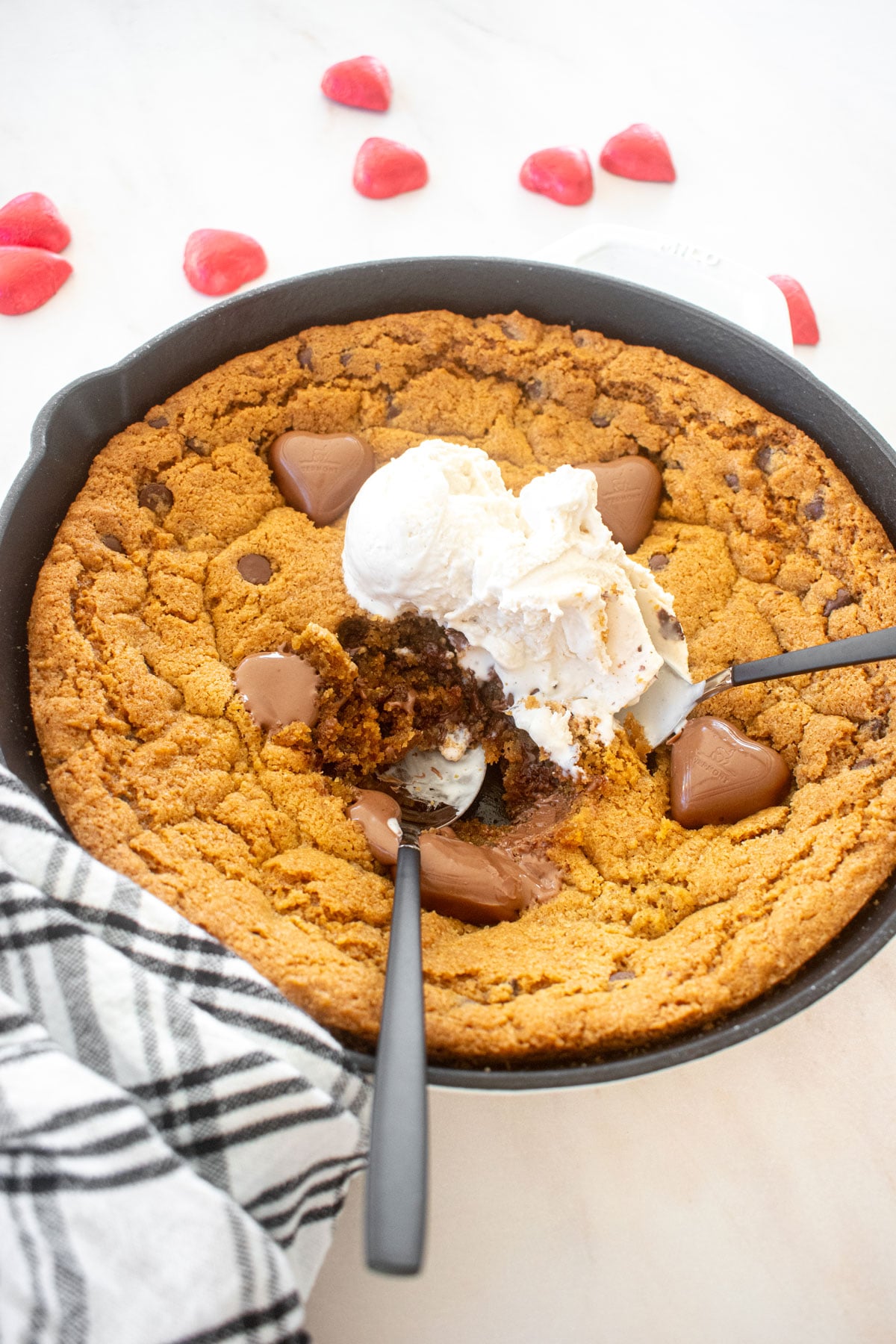 valentine's day peanut butter cookie skillet with vanilla ice cream and spoons on a marble counter.