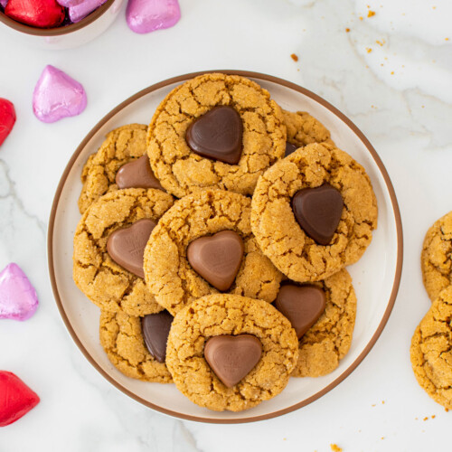 valentine's peanut butter blossoms on a plate on a marble counter with red and pink chocolate wrapped hearts.