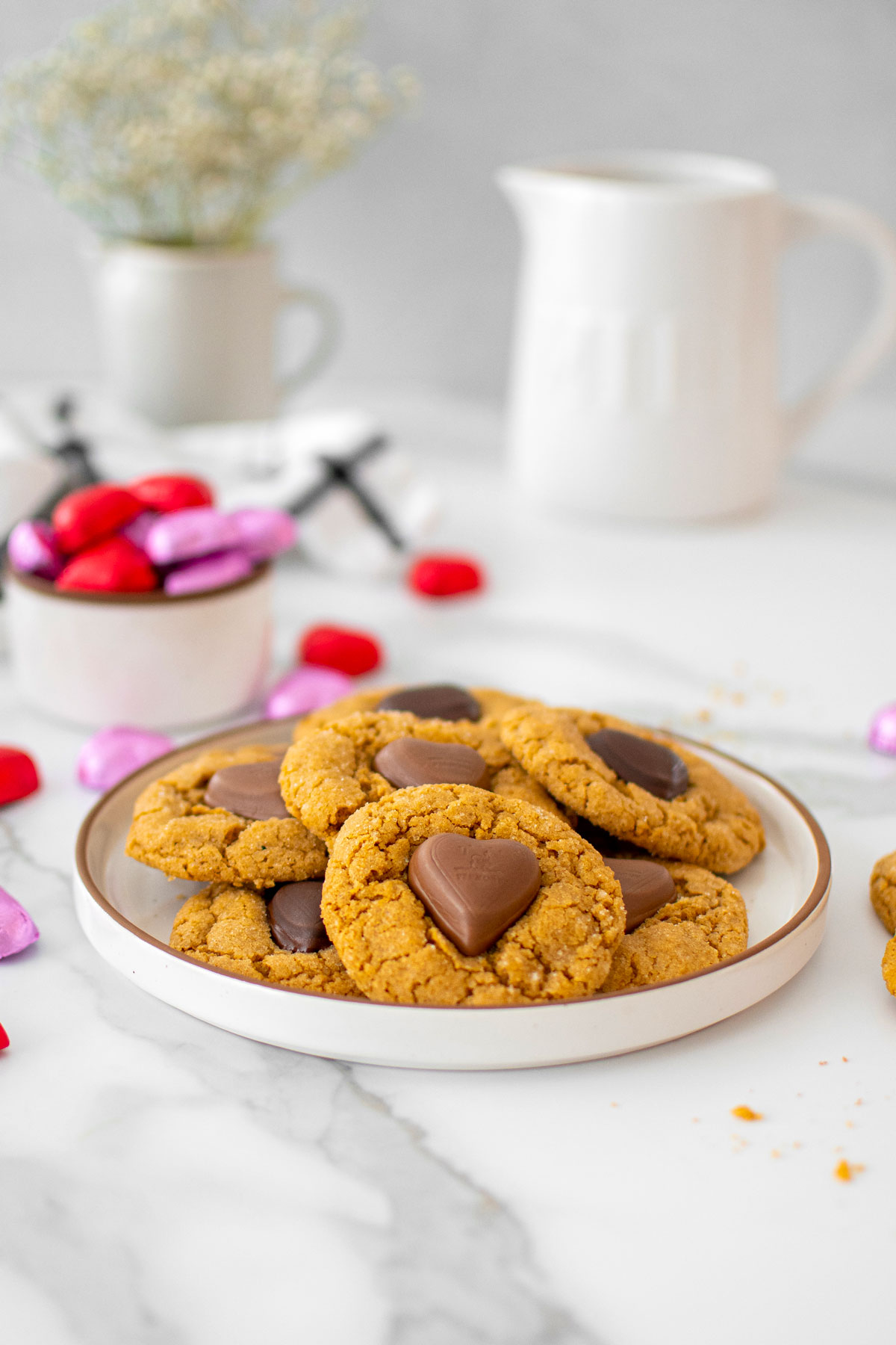 valentine's peanut butter blossoms on a plate on a marble counter with red and pink chocolate wrapped hearts.