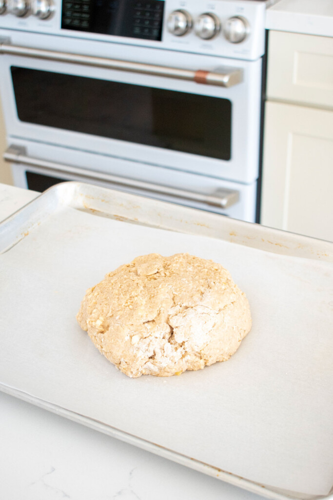 banana scones dough formed into a disk on a baking sheet on a marble kitchen counter.