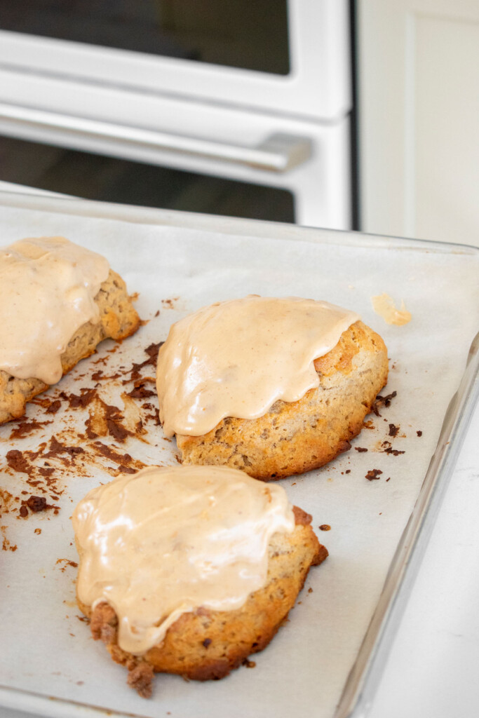 banana scones with peanut butter glaze on a baking sheet on a white marble counter.