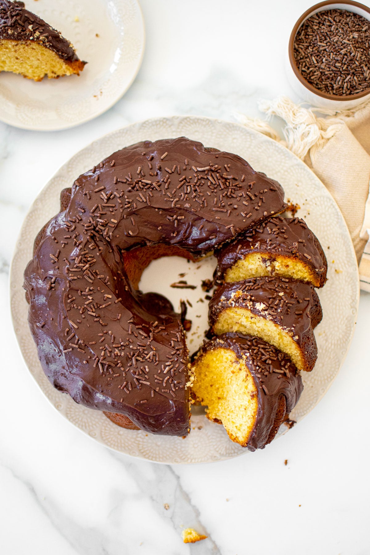 chocolate donut pound cake cut into slices on a white cake plate on a marble table.