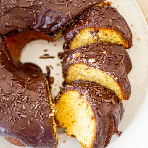 chocolate donut pound cake cut into slices on a white cake plate on a marble table.