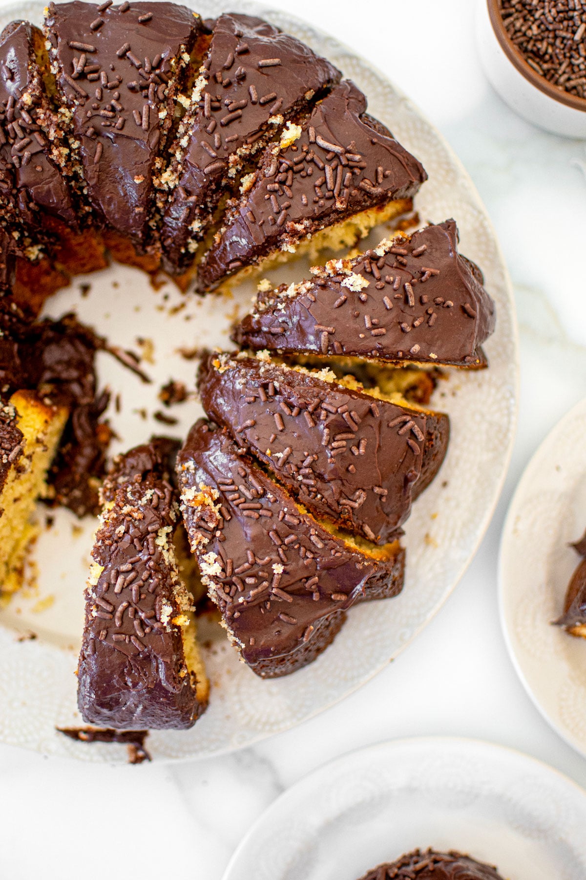 chocolate donut pound cake cut into slices on a white cake plate on a marble table.
