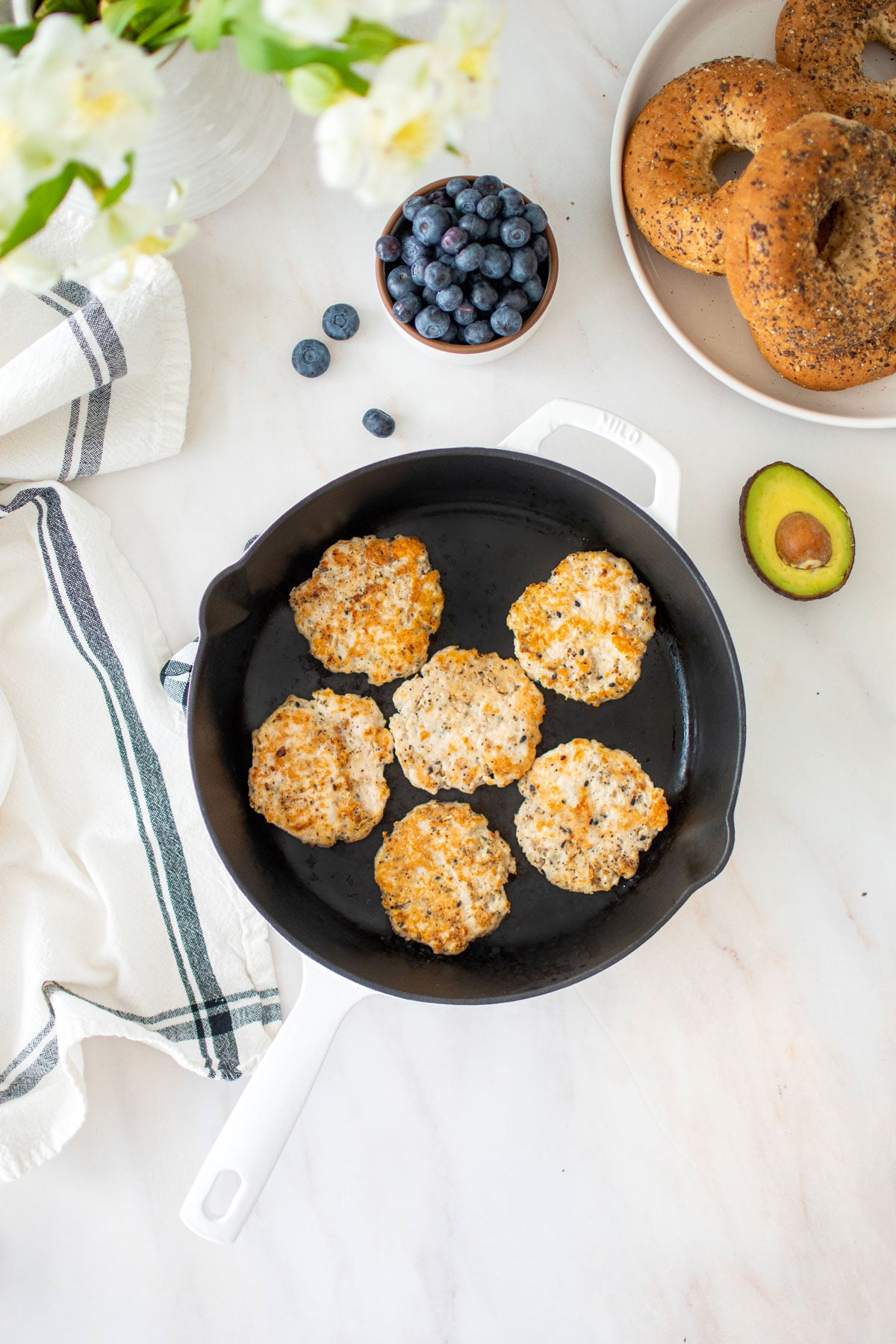 everything bagel turkey breakfast sausages in a cast iron skillet with a bowl of blueberries, bagels and avocado.