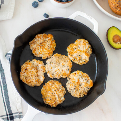 everything bagel turkey breakfast sausages in a cast iron skillet with a bowl of blueberries, bagels and avocado.