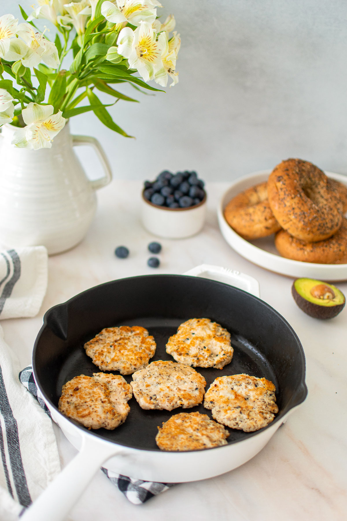 everything bagel turkey breakfast sausages in a cast iron skillet with a bowl of blueberries, bagels and avocado.