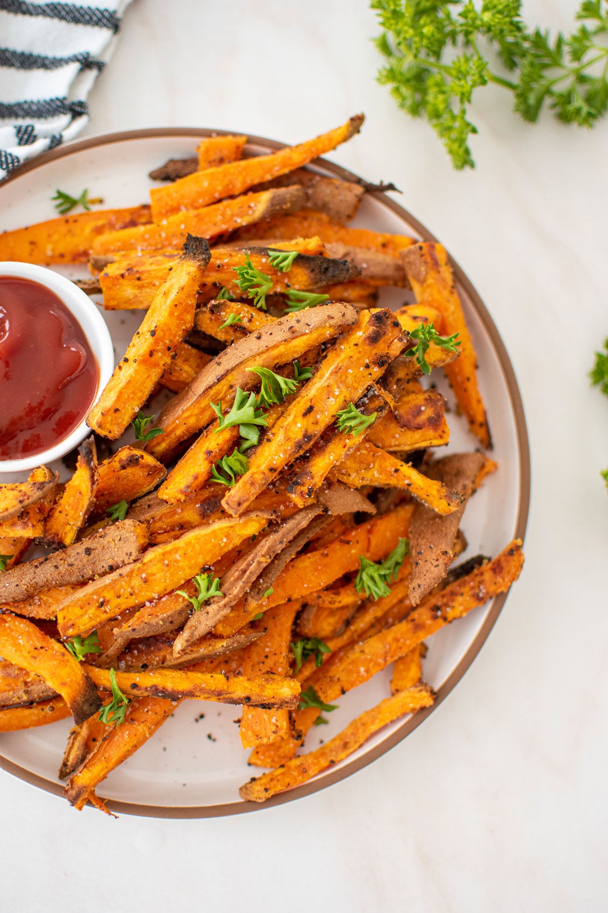 garlic lemon sweet potato fries with fresh parsley on a plate with a dish of ketchup.