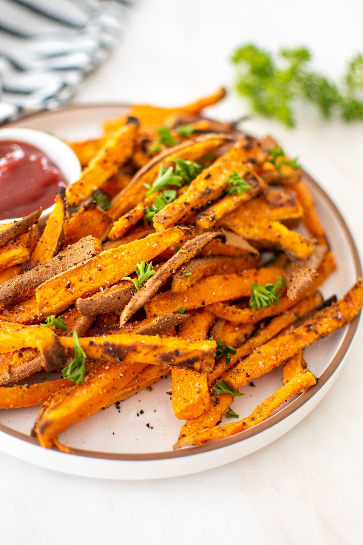 garlic lemon sweet potato fries with fresh parsley on a plate with a dish of ketchup.
