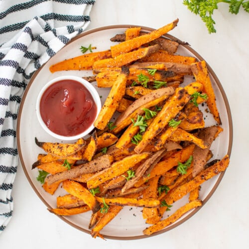 garlic lemon sweet potato fries with fresh parsley on a plate with a dish of ketchup.
