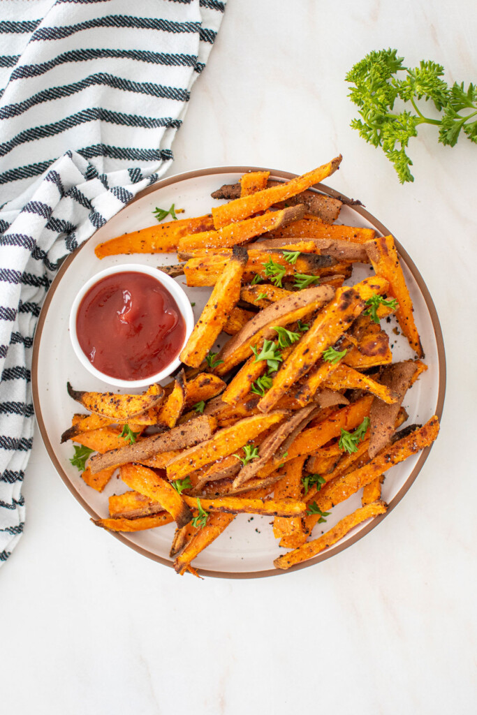 garlic lemon sweet potato fries with fresh parsley on a plate with a dish of ketchup.