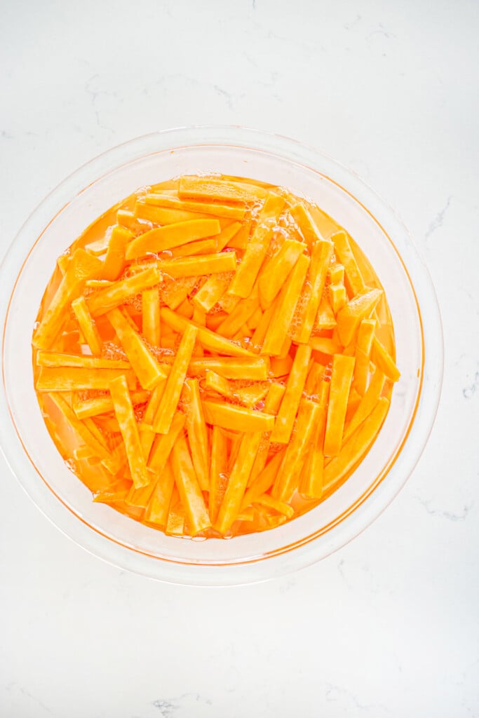 sweet potato fries soaking in a glass mixing bowl on a marble countertop.
