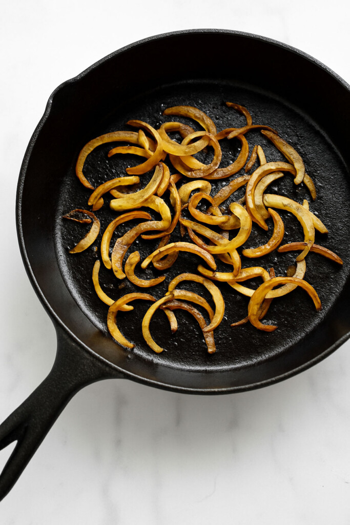 grilled onions in a cast iron skillet on a white marble countertop.