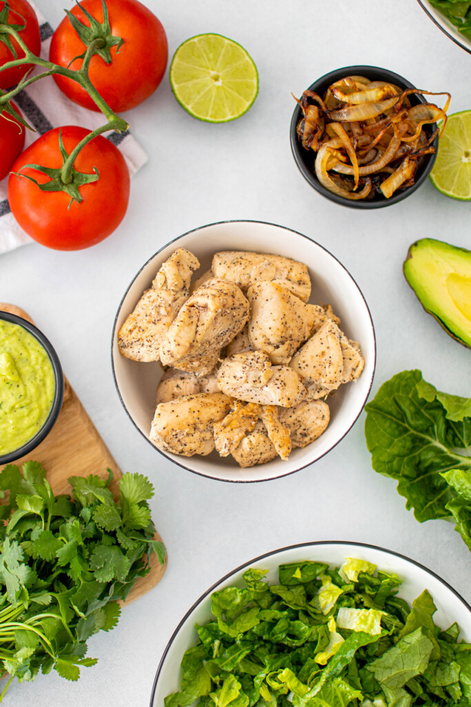 garlic lime chicken in a small bowl with lettuce, tomato and avocado getting prepped for salad.