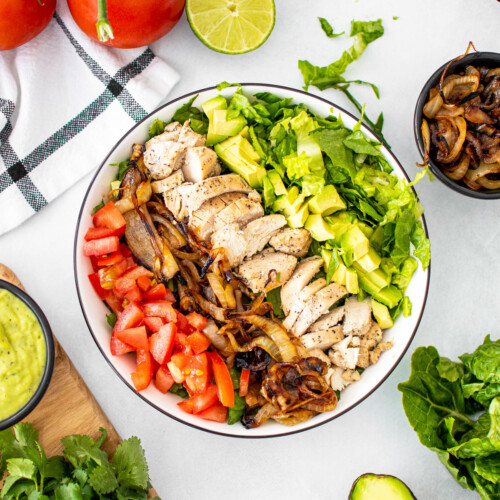 garlic lime chicken taco salad in a big bowl on a gray countertop with fresh ingredients around.