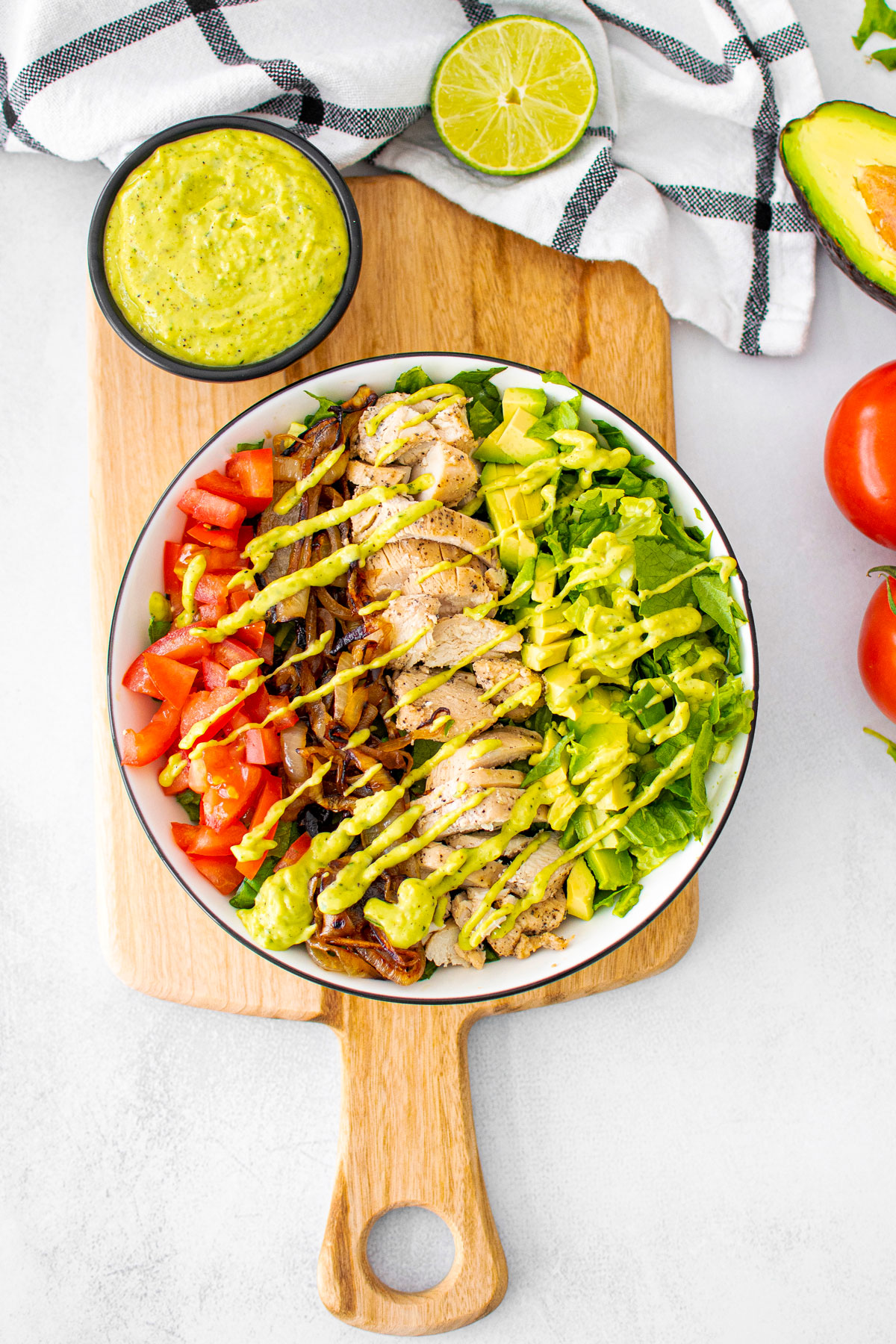 garlic lime chicken taco salad with creamy avocado dressing in a bowl on a wood cutting board.
