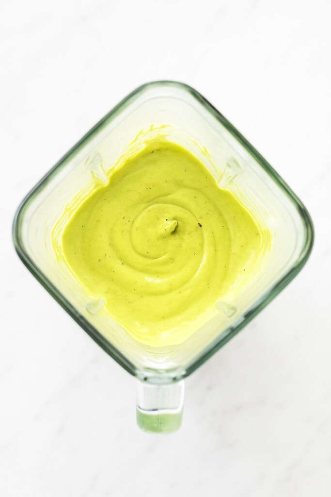 creamy avocado lime dressing mixed together in a glass blender on a white marble countertop.
