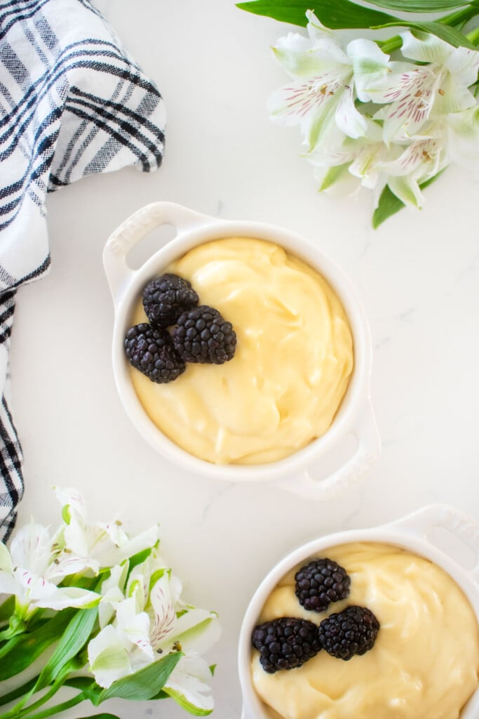 homemade vanilla malt pudding in a mini white dutch oven with fresh blackberries on a white marble counter with flowers.