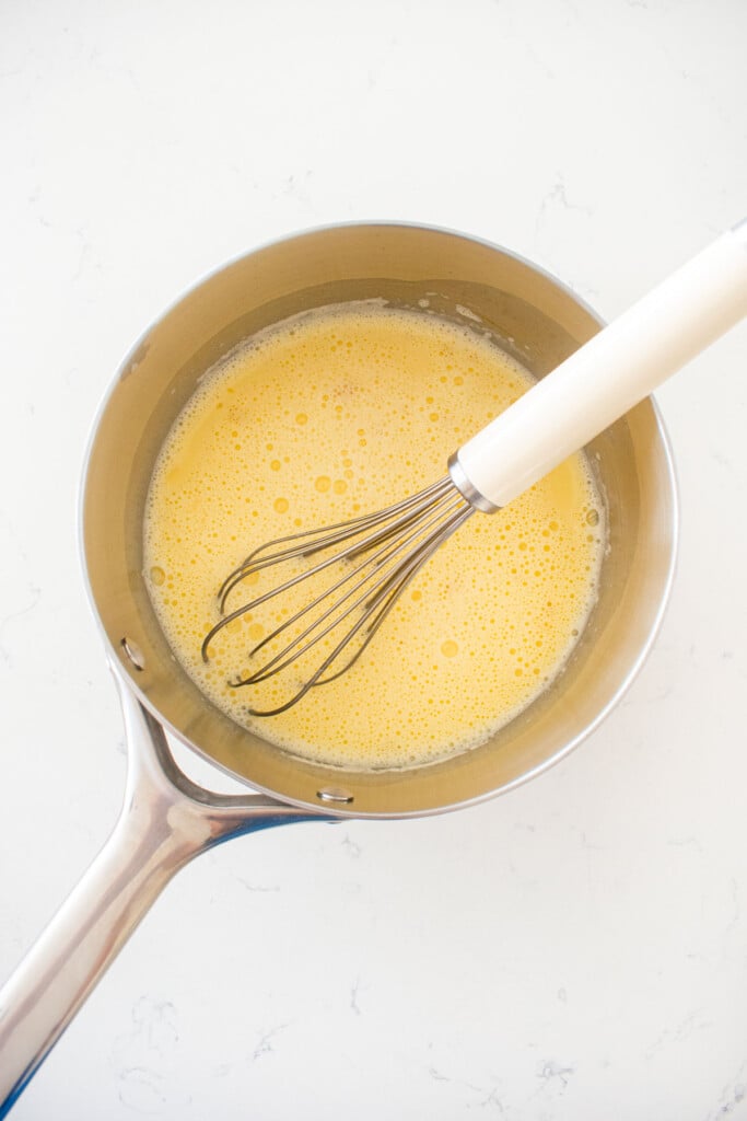 stainless steel pot with egg yolks whisked with milk on a white marble counter.