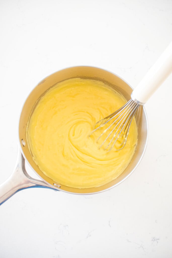homemade vanilla pudding being whisked together in a pot on a white marble conter.