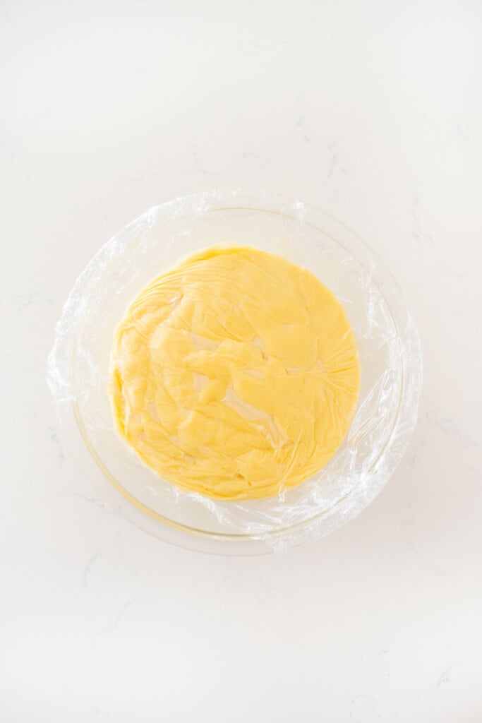 homemade vanilla malt pudding in a glass mixing bowl with plastic wrap pressed against it.